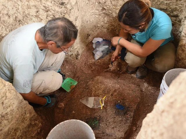 Man and woman crouch in a square archaeological dig pit, looking at something on the dirt