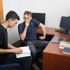 A professor and student sit together at a desk while the student holds a book and they are talking